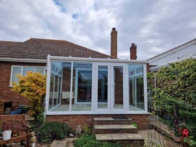 White uPVC conservatory with full-height glazing and French doors, installed at rear of a bungalow with steps to garden.