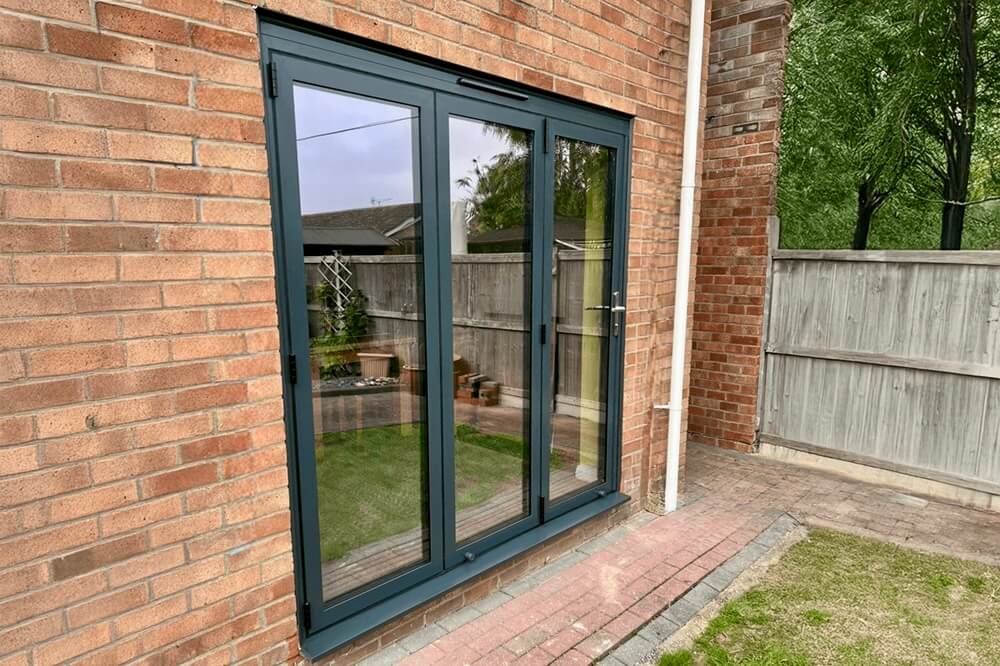 Black aluminium bifold doors installed in a brick-built home, providing a secure and energy-efficient transition to an outdoor garden space.