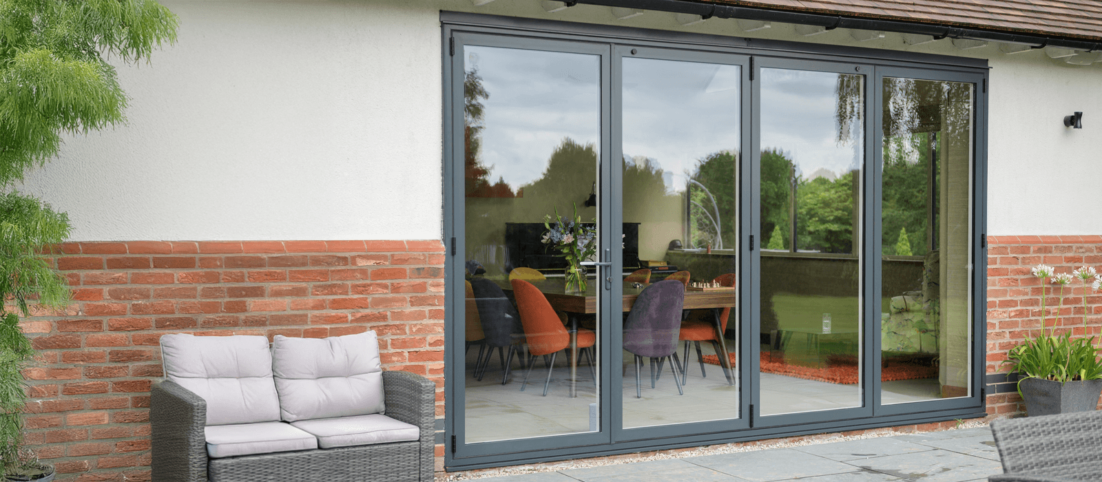Sheerline grey aluminium bifold doors providing a modern connection between an indoor dining area and an outdoor patio.