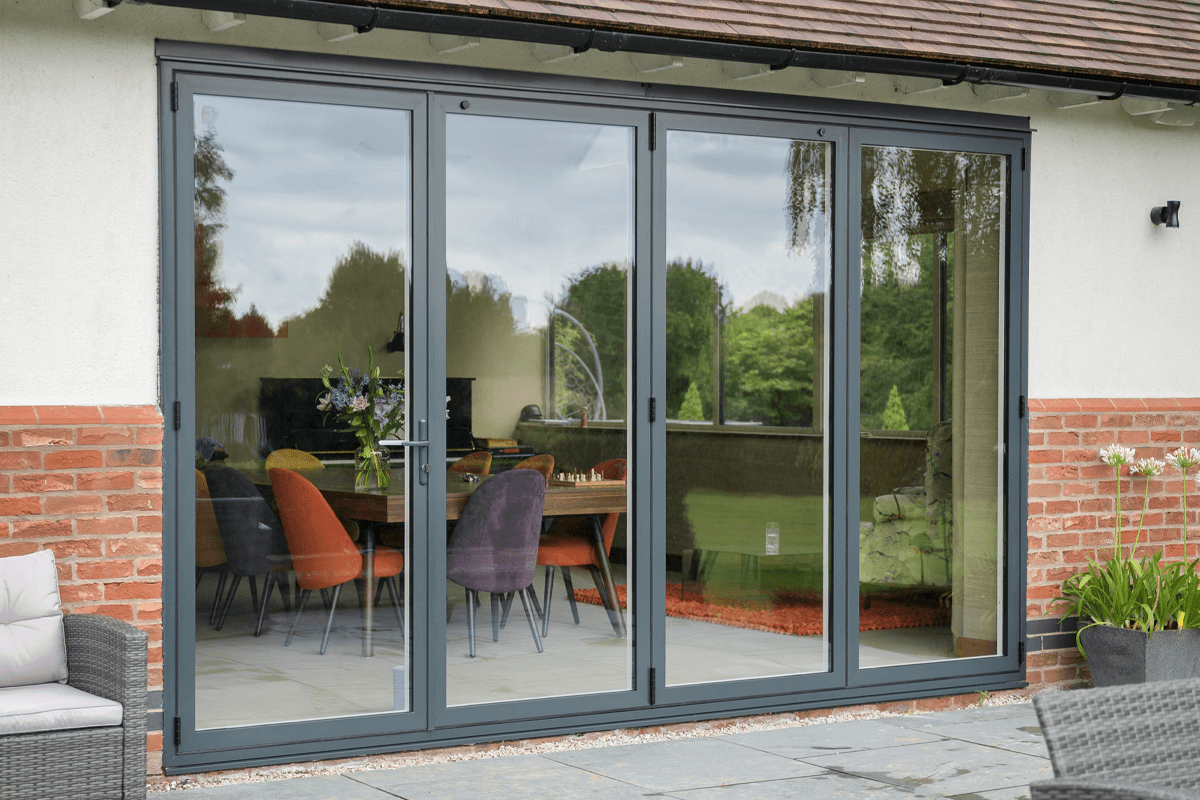 Sheerline grey aluminium bifold doors providing a modern connection between an indoor dining area and an outdoor patio.