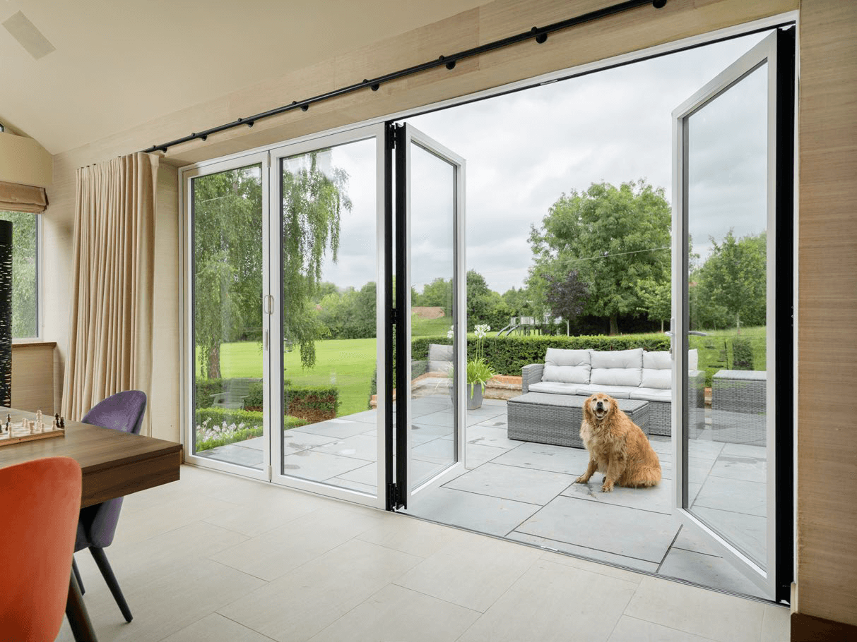 White sheerline bifold doors fully open, connecting a modern interior to an outdoor patio with a garden view.