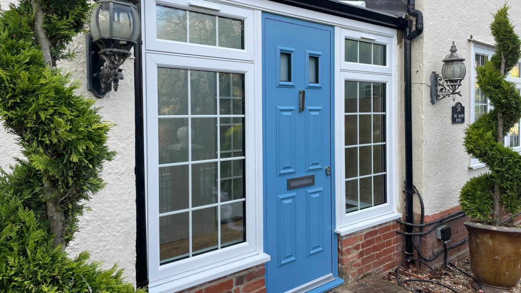 Blue composite entrance door with sidelights and white flush sash windows featuring decorative Georgian bars in a brick-built home.
